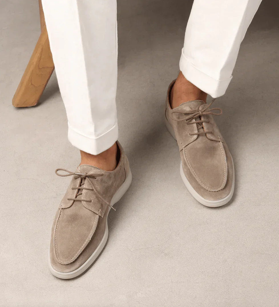 Light beige suede lace-up loafers on feet with white pants