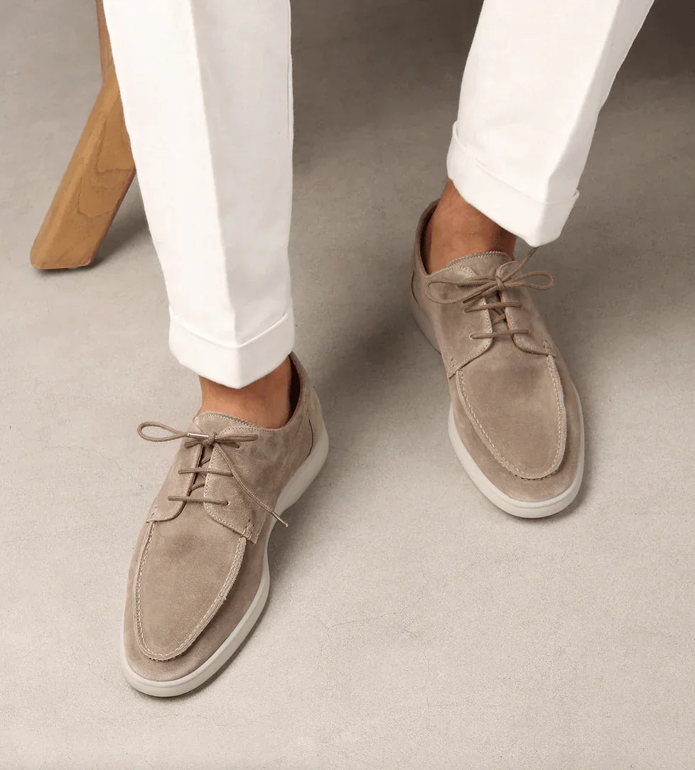 Light beige suede lace-up loafers on feet with white pants