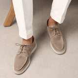 Light beige suede lace-up loafers on feet with white pants