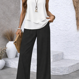 White sleeveless tiered top with black palazzo pants, standing close-up