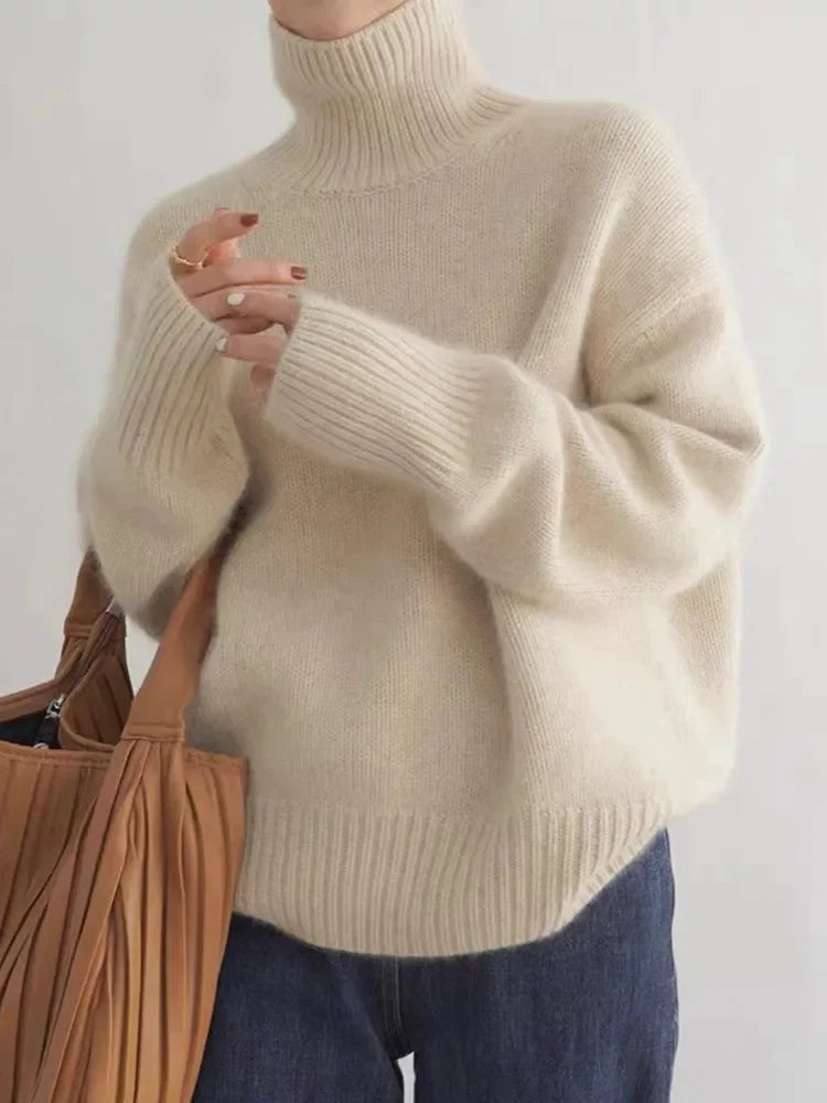 Beige turtleneck knit sweater with ribbed cuffs and hem, worn with dark jeans.