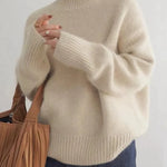 Beige turtleneck knit sweater with ribbed cuffs and hem, worn with dark jeans.