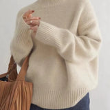Beige turtleneck knit sweater with ribbed cuffs and hem, worn with dark jeans.