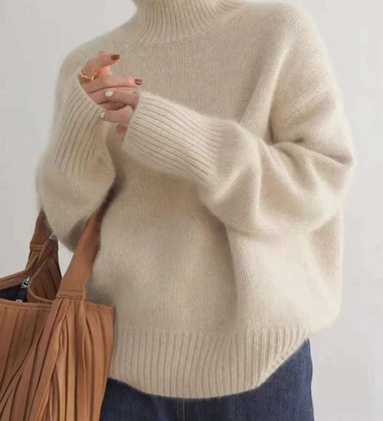 Beige turtleneck knit sweater with ribbed cuffs and hem, worn with dark jeans.