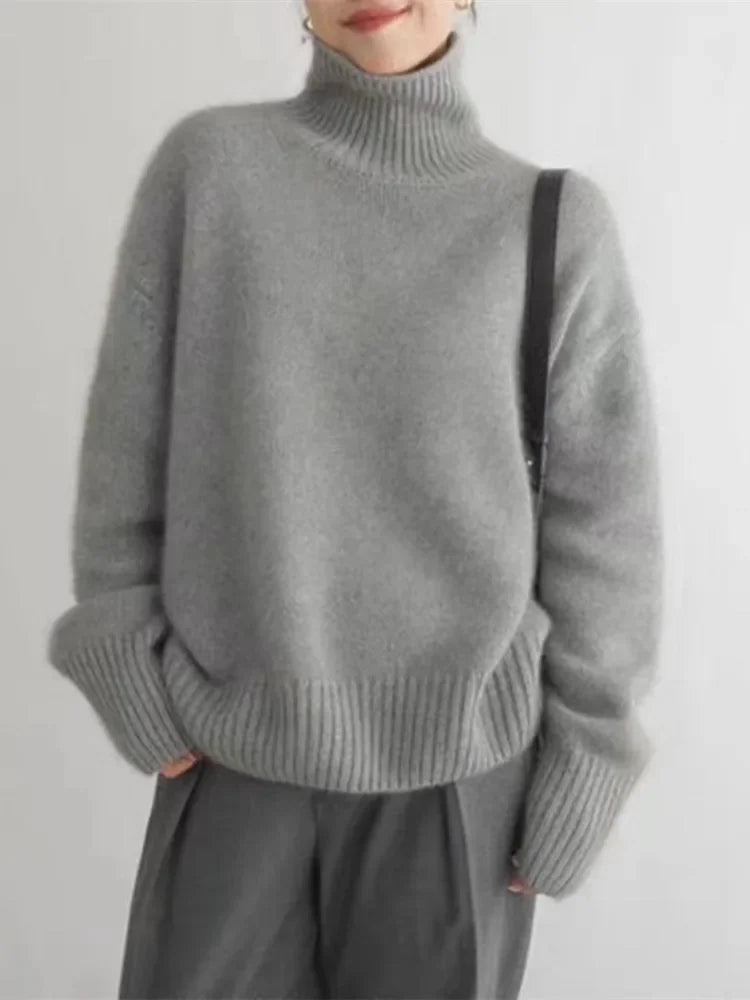 Gray turtleneck knit sweater with ribbed cuffs and relaxed fit, worn with a skirt.