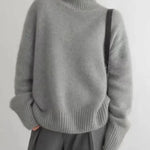 Gray turtleneck knit sweater with ribbed cuffs and relaxed fit, worn with a skirt.
