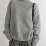 Gray turtleneck knit sweater with ribbed cuffs and relaxed fit, worn with a skirt.