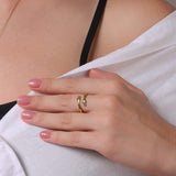 Gold wave-detail ring on a hand with pink nail polish