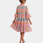 Back view of printed midi dress with tiered skirt and bell sleeves in pink, orange, and greenish