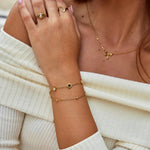 Gold chain bracelet with small black and white round stone charm at wrist