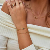 Gold chain bracelet with small black and white round stone charm at wrist