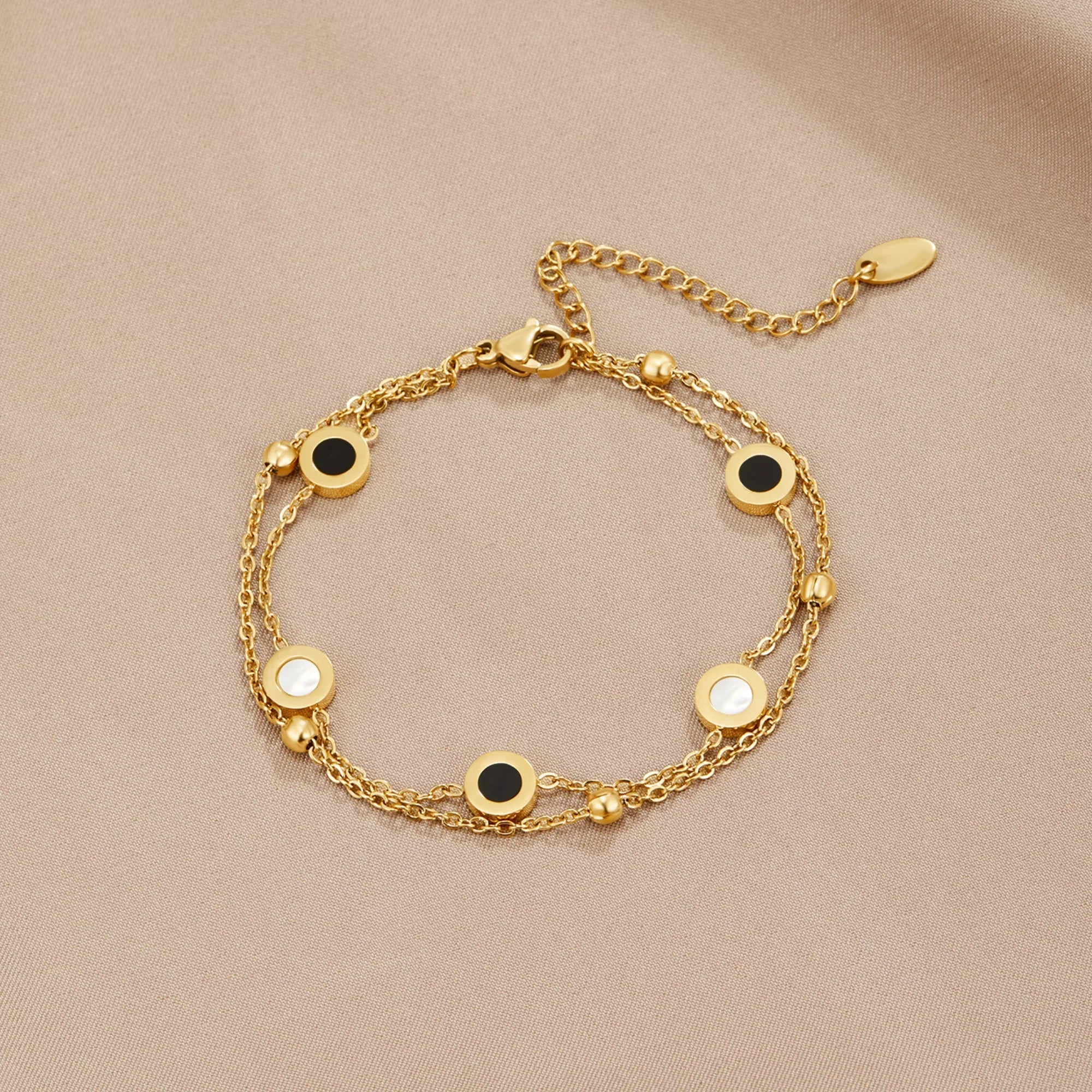 Gold chain bracelet with alternating black and white round stone discs on clasp side