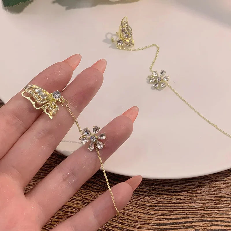 Gold butterfly and flower ear cuff on hand, dangling chain with rhinestone studs