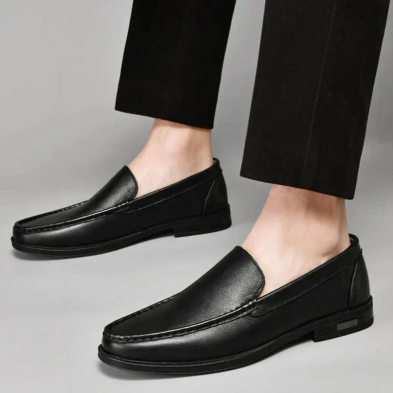 Black leather loafers on feet, slip-on style with moc toe stitching and low heel