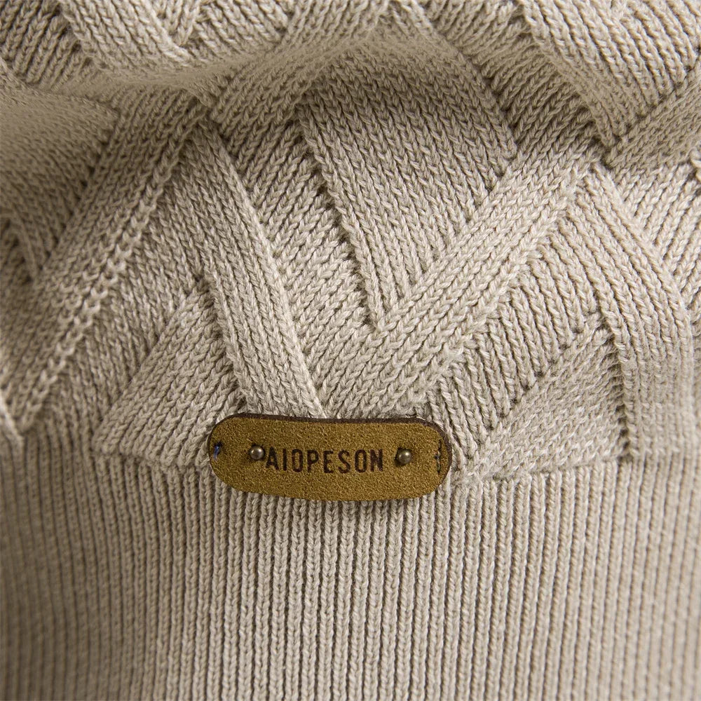 Beige knit sweater close-up with diamond texture and leather-look logo patch