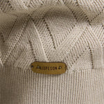 Beige knit sweater close-up with diamond texture and leather-look logo patch