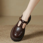 Brown T-bar loafers with gold buckle, T-strap cutout, and treaded sole
