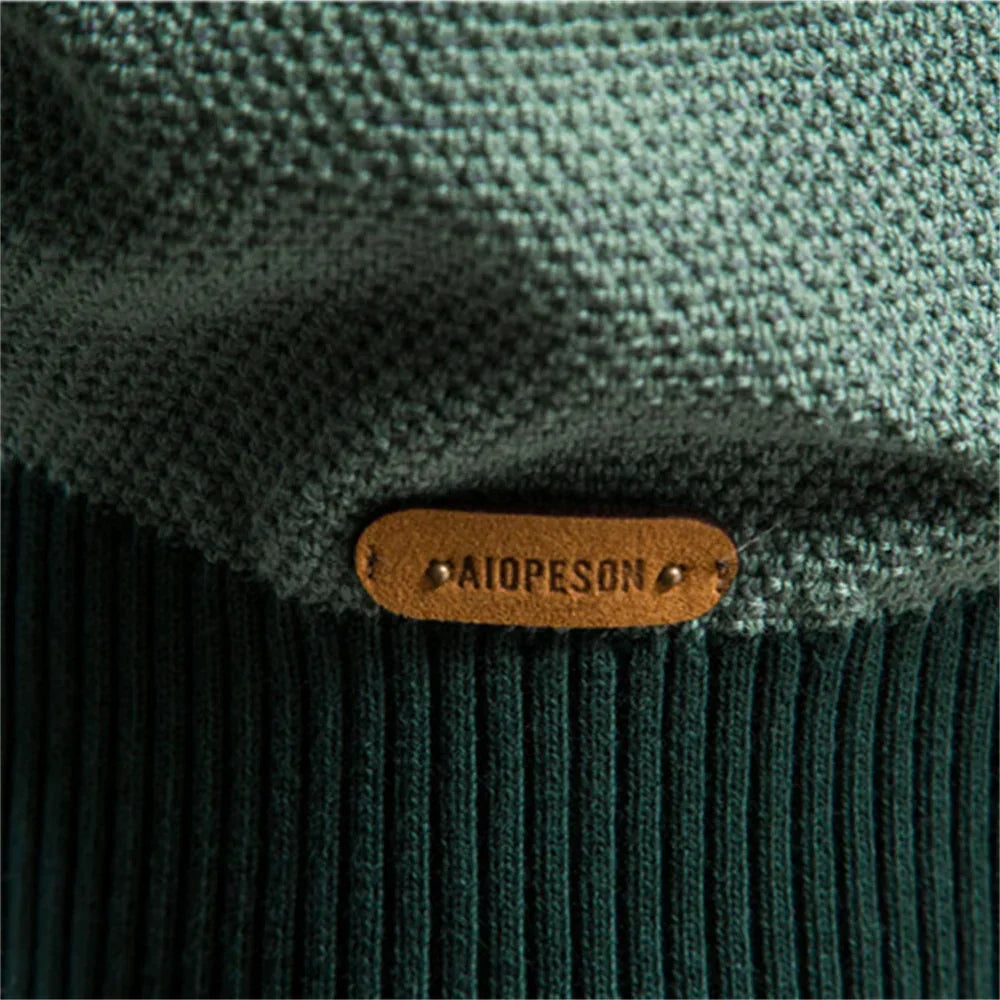 Leather-look brand patch on dark green ribbed sweater hem