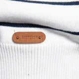 Brand leather patch on white knit sweater with navy striped bands, small metal studs