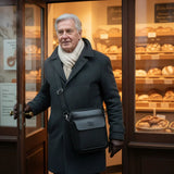 Black leather shoulder bag with front flap, logo emblem, and adjustable strap
