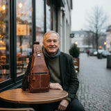 Brown leather chest bag on tabletop with front zip pocket and adjustable strap