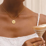Gold coin pendant necklace on neckline with small round medallion charm