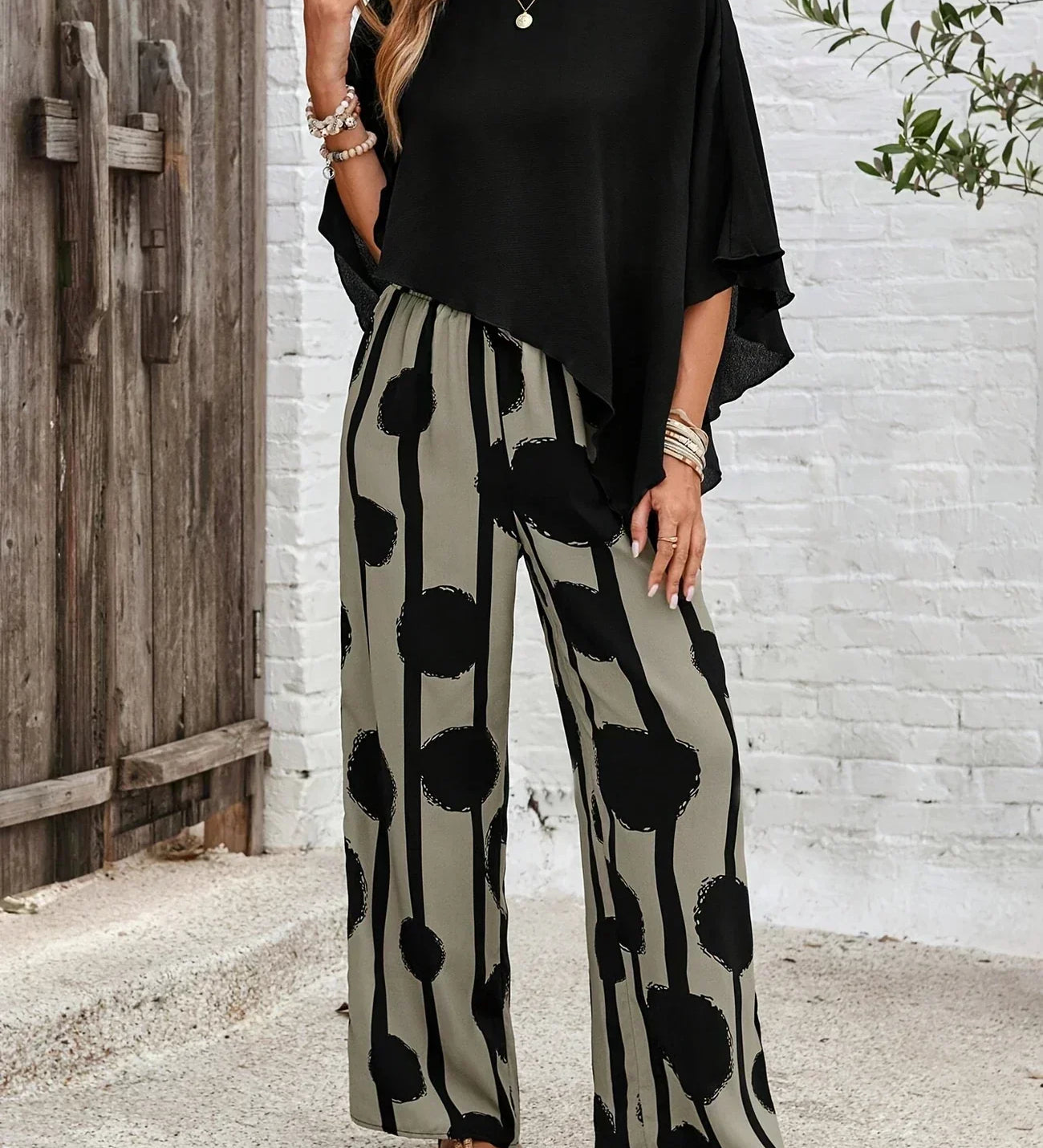 Black asymmetrical top with draped sleeves paired with wide-leg boho pants, black-on-cream dot print