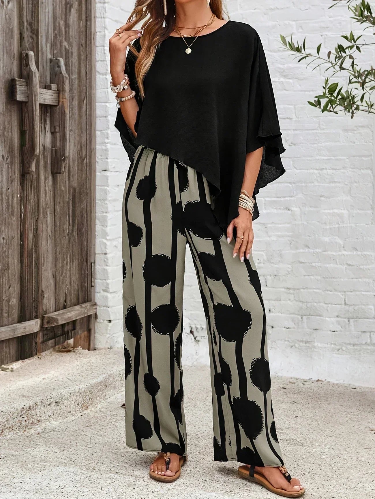 Black asymmetrical top with draped sleeves paired with wide-leg boho pants, black-on-cream dot print