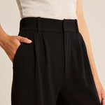 Close-up of black trousers waistband with belt loops, button closure, and pleats