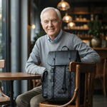 Black leather backpack on chair with shoulder straps and front buckle hardware