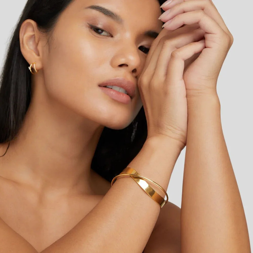 Gold cuff bracelet with smooth wide band and diagonal centerpiece on model’s arm.