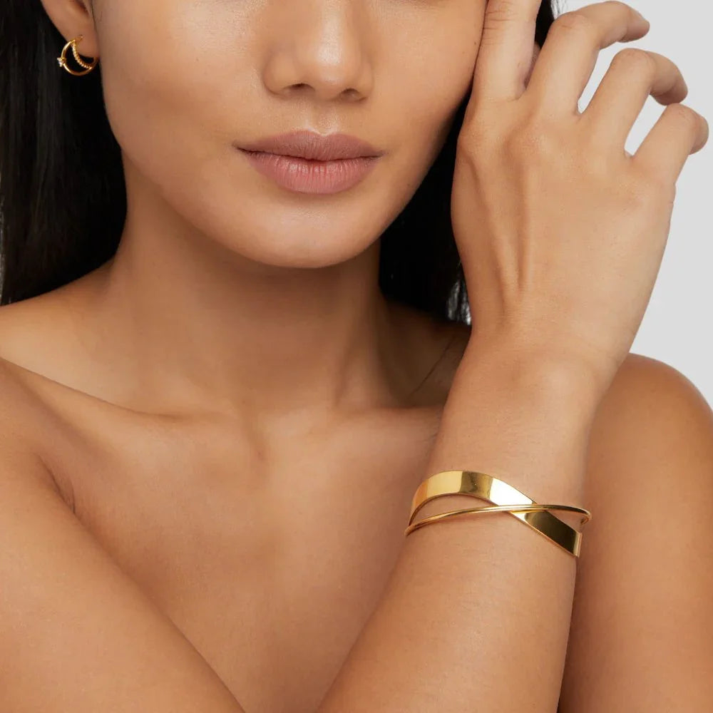 Gold cuff bracelet close-up with wide open band and diagonal geometric detail.