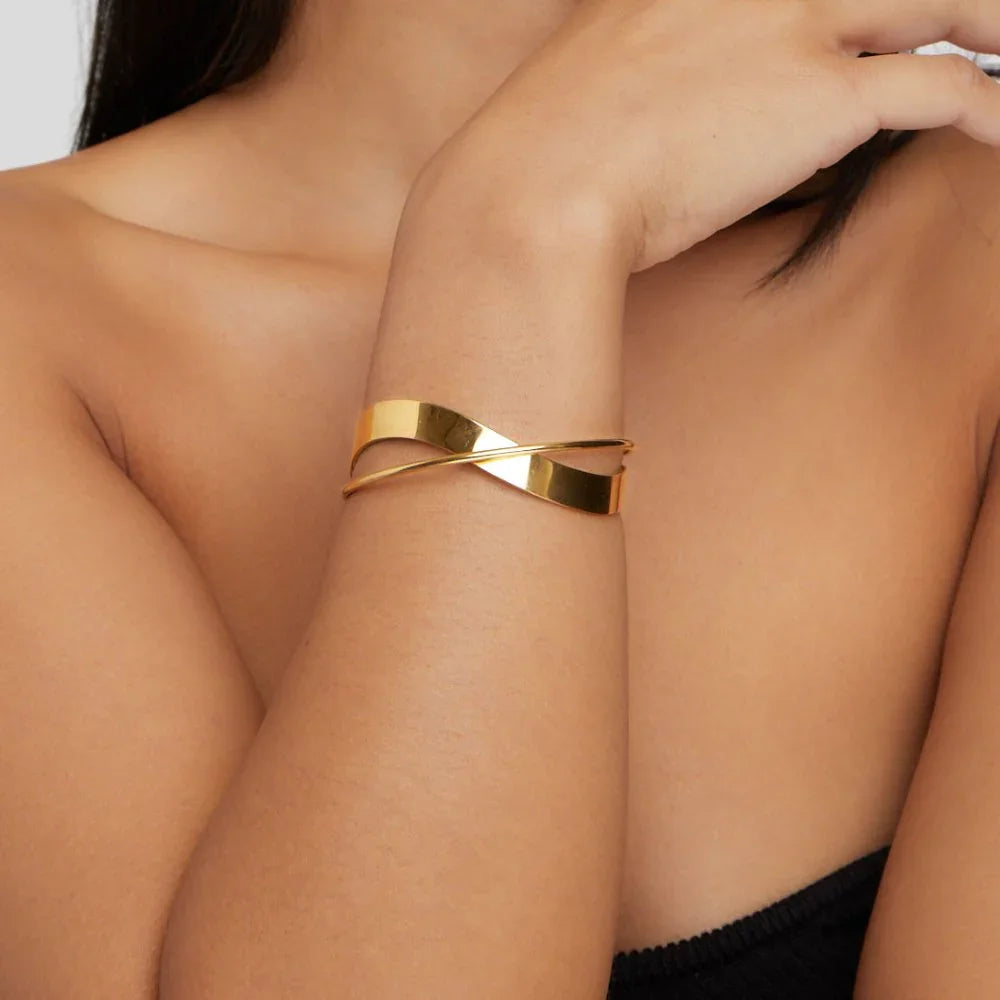 Gold cuff bracelet on wrist, featuring a wide curved band with diagonal bar.