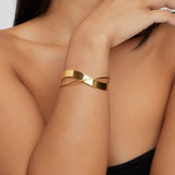 Gold cuff bracelet on wrist, featuring a wide curved band with diagonal bar.