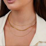 Gold multi-layer chain necklace worn at neckline, layered smooth links