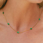 Gold chain necklace with small green rectangular stones spaced along the thin chain.