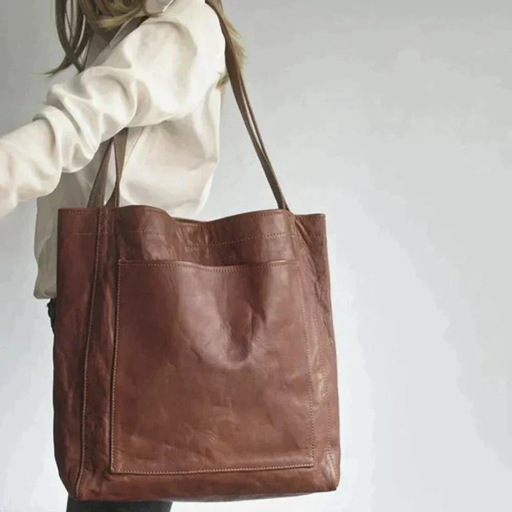 Dark brown leather tote bag held by model, open top with dual handles