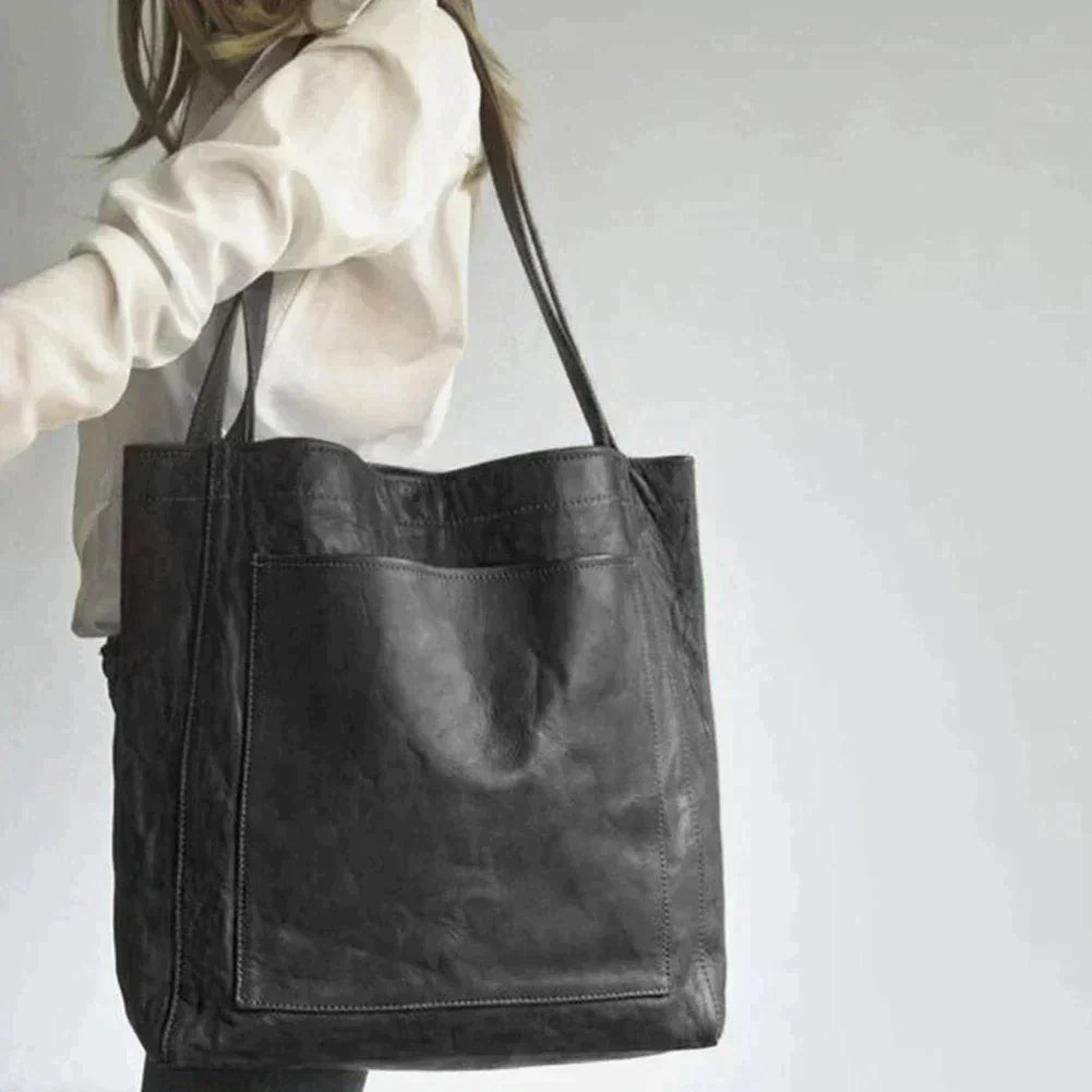 Black leather tote bag held by model, open top with dual handles