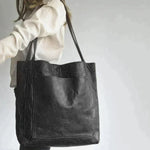 Black leather tote bag held by model, open top with dual handles