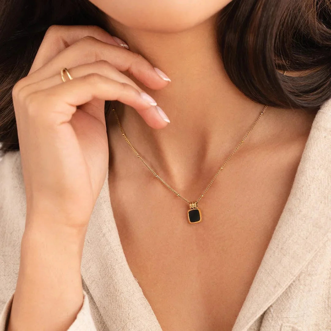 Gold pendant necklace worn at collarbone with black square charm