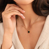 Gold pendant necklace worn at collarbone with black square charm