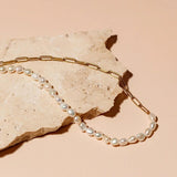 Gold link and pearl necklace laid on a stone surface