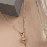 Gold long chain pendant necklace with round crystal-like centerpiece and tassel drops
