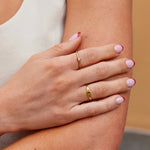 Gold ring with small clear stone on finger, stacked with gold bands