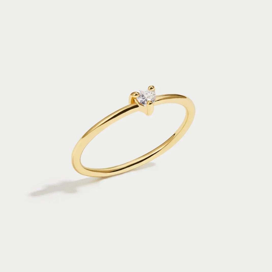 Gold ring with smooth band and small clear stone at center, angled view