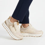 Beige women’s comfort sneakers with zip detail, white laces, and cushioned sole