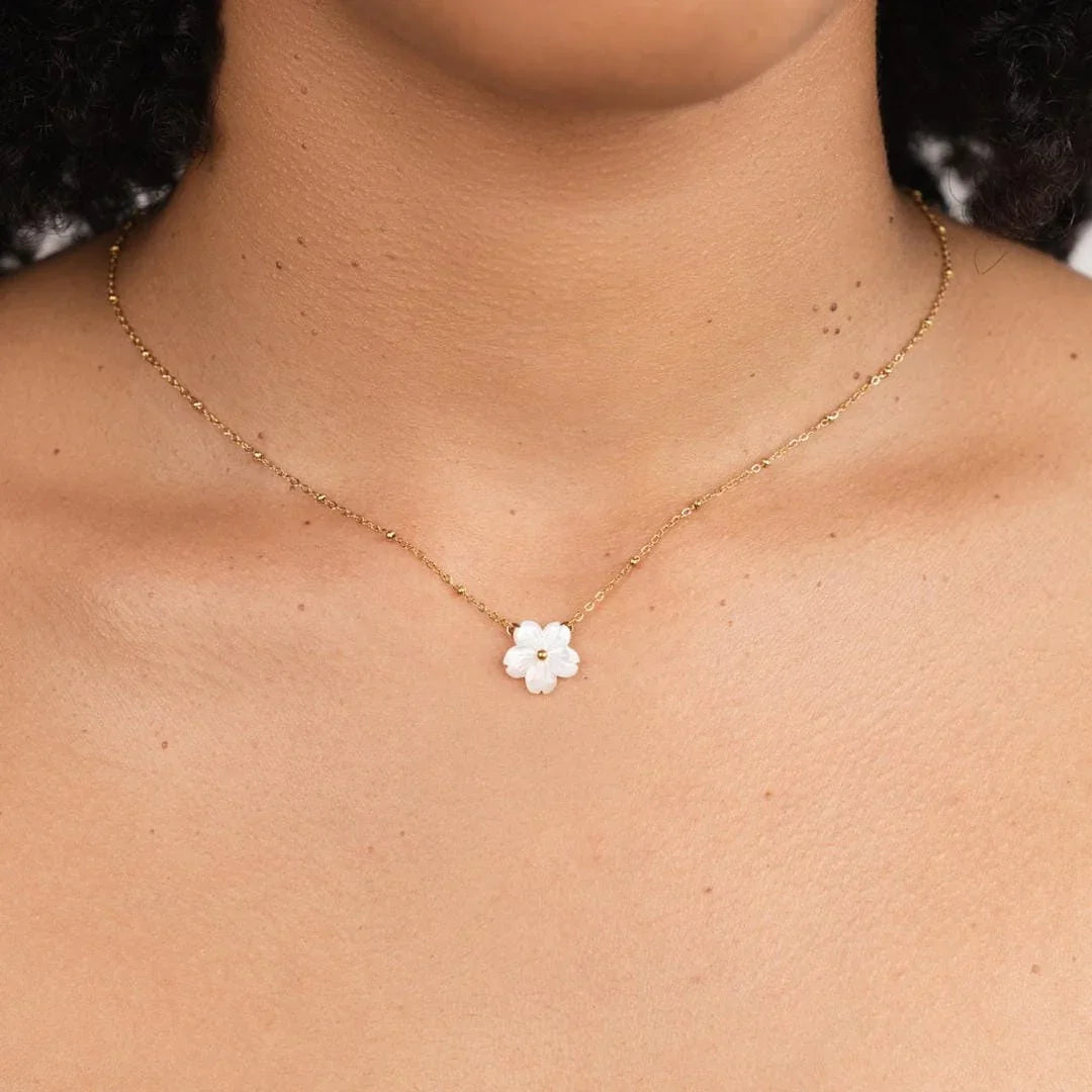 Gold chain necklace with small white flower pendant at center