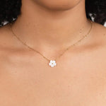 Gold chain necklace with small white flower pendant at center