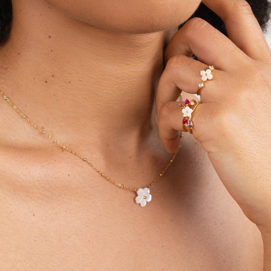 Gold flower pendant necklace with white bloom, displayed on neckline